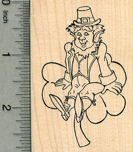 A wooden rubber stamp featuring a Leprechaun in hat sitting on a four leaf clover with a smile.